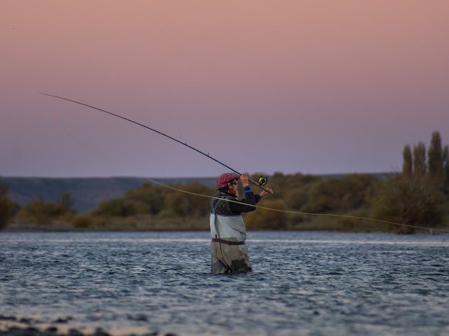 Pescador lanzando con mosca al atardecer