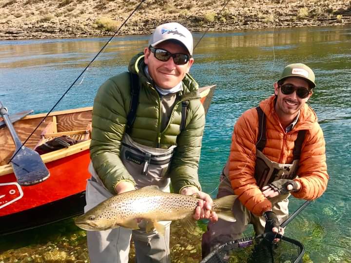 Dos pescadores mostrando una trucha marrón junto al bote